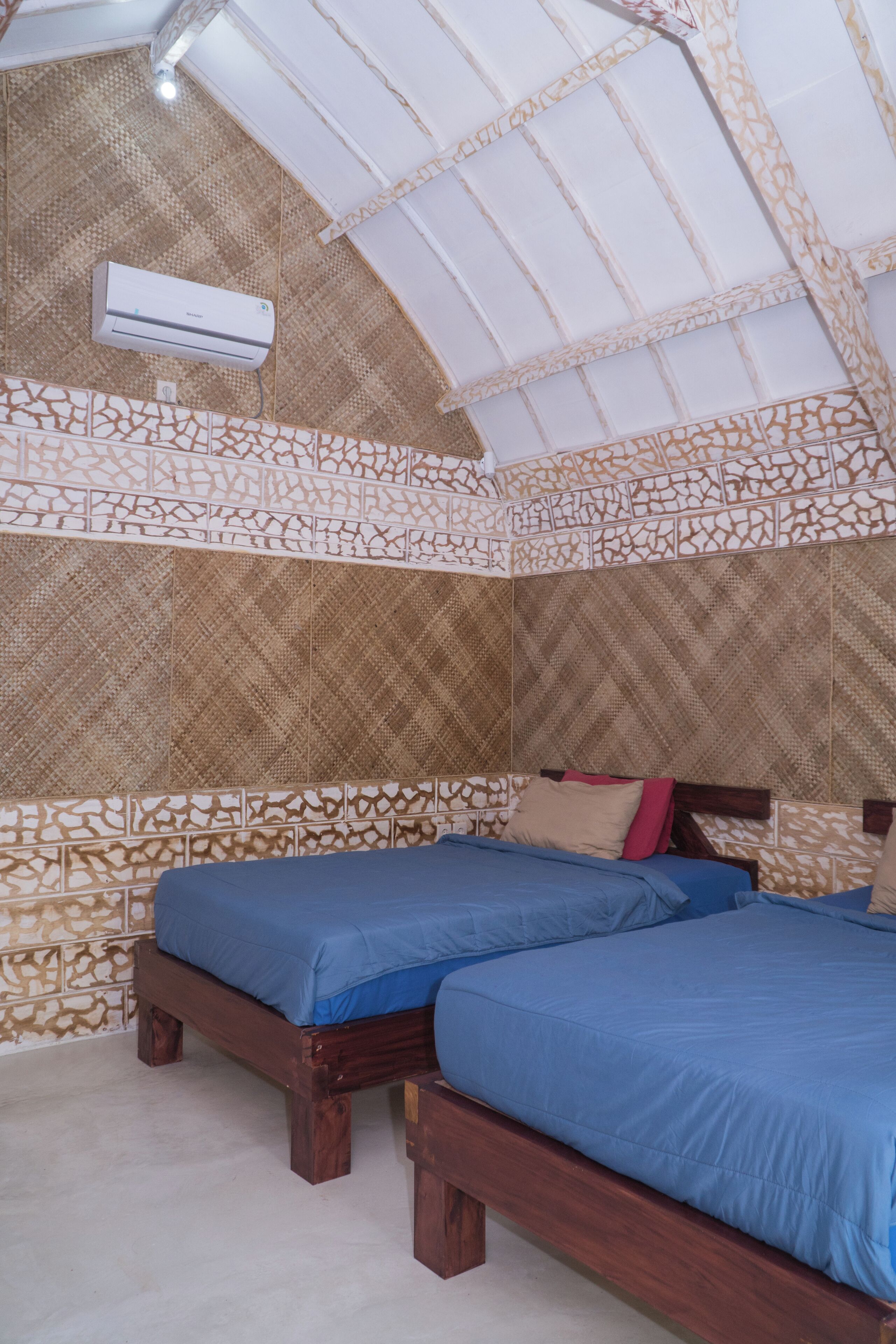 Quarto com duas camas de madeira, paredes estampadas e um aparelho de ar condicionado.