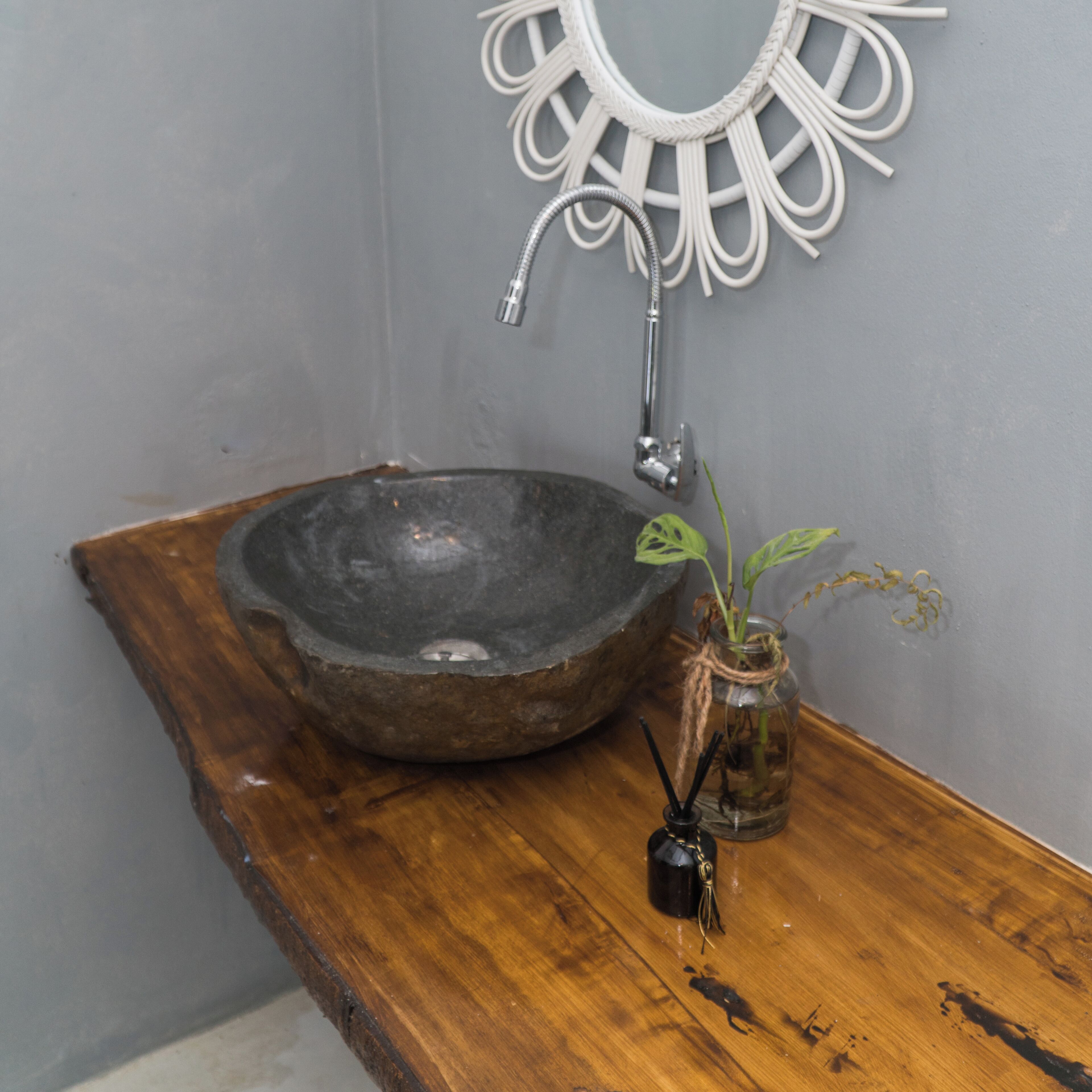 Un tocador rústico de madera con un lavabo de piedra, una pequeña planta en maceta y un llavero negro.