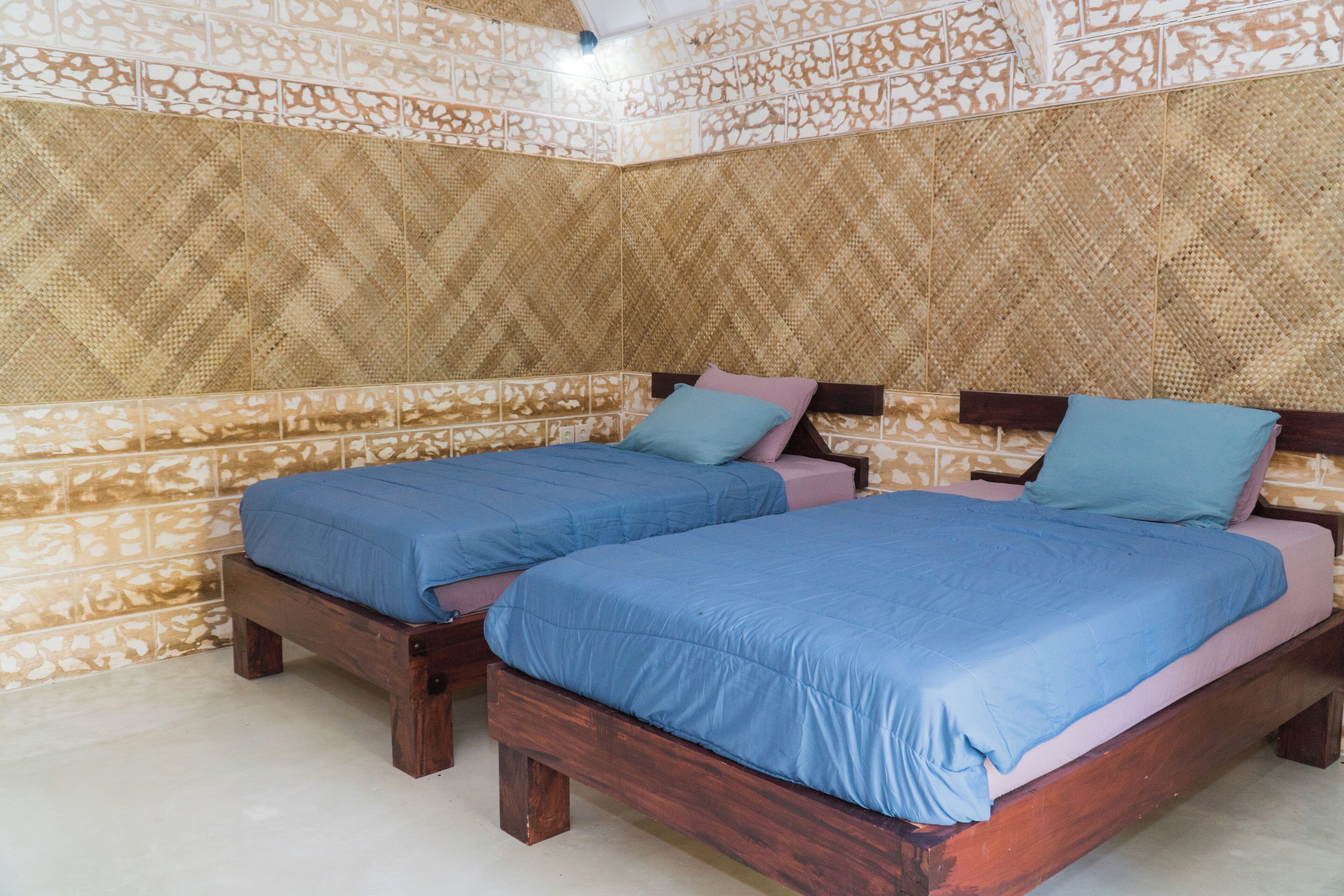 Una habitación con dos camas de madera, cada una con ropa de cama azul y almohadas rosas. Las paredes tienen un diseño estampado.