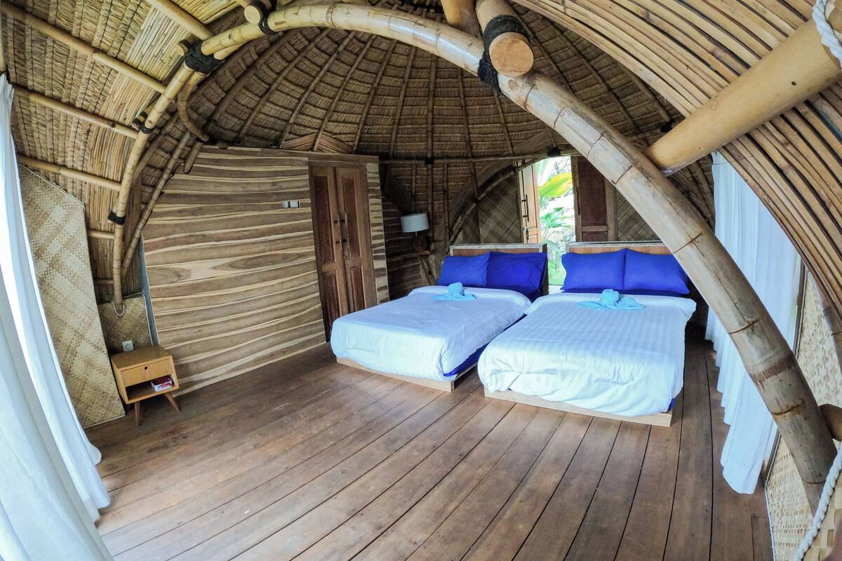 Une chambre avec deux lits, un plancher en bois et un toit de chaume.