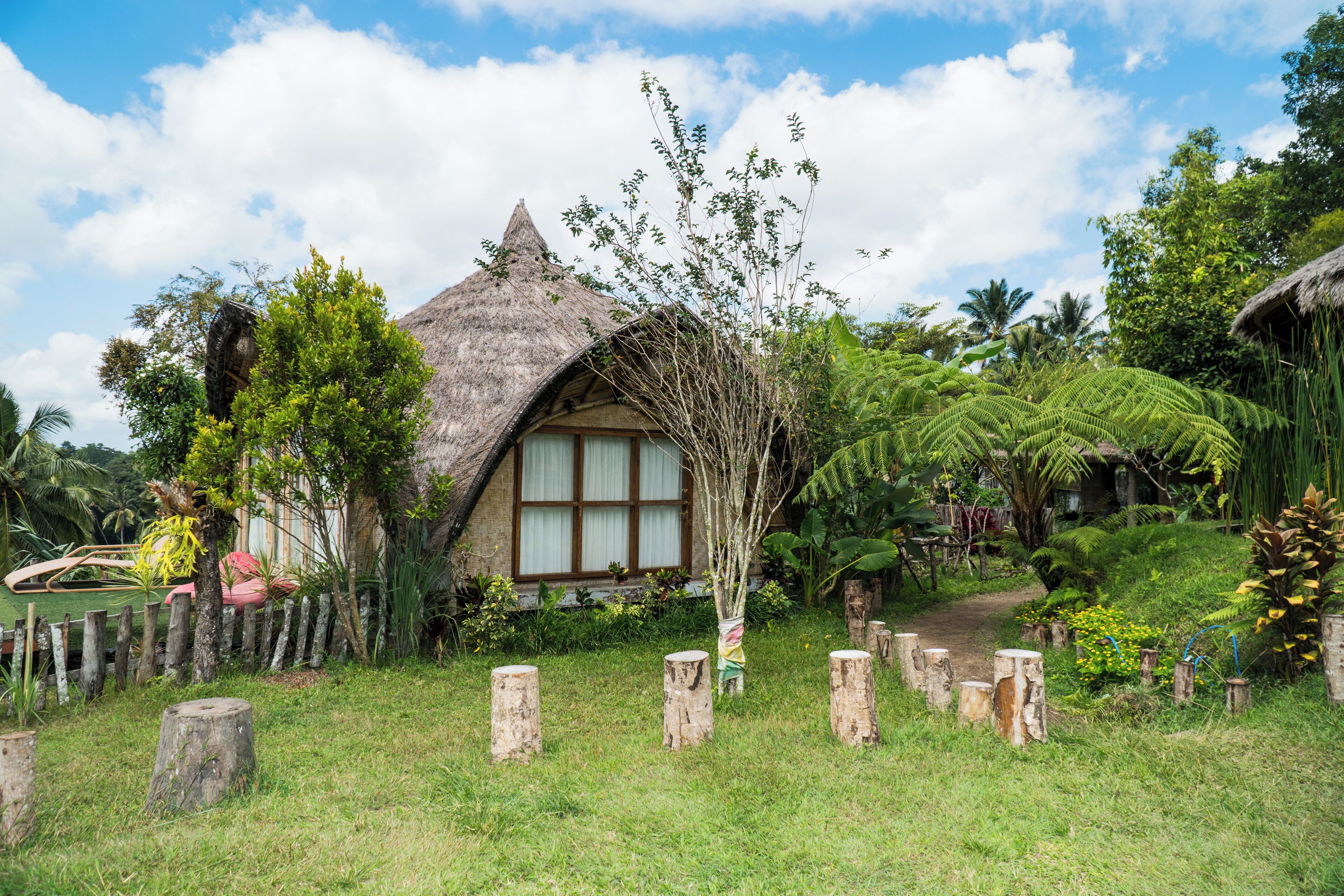 A thatched-roof house surrounded by lush greenery and a clear sky.
