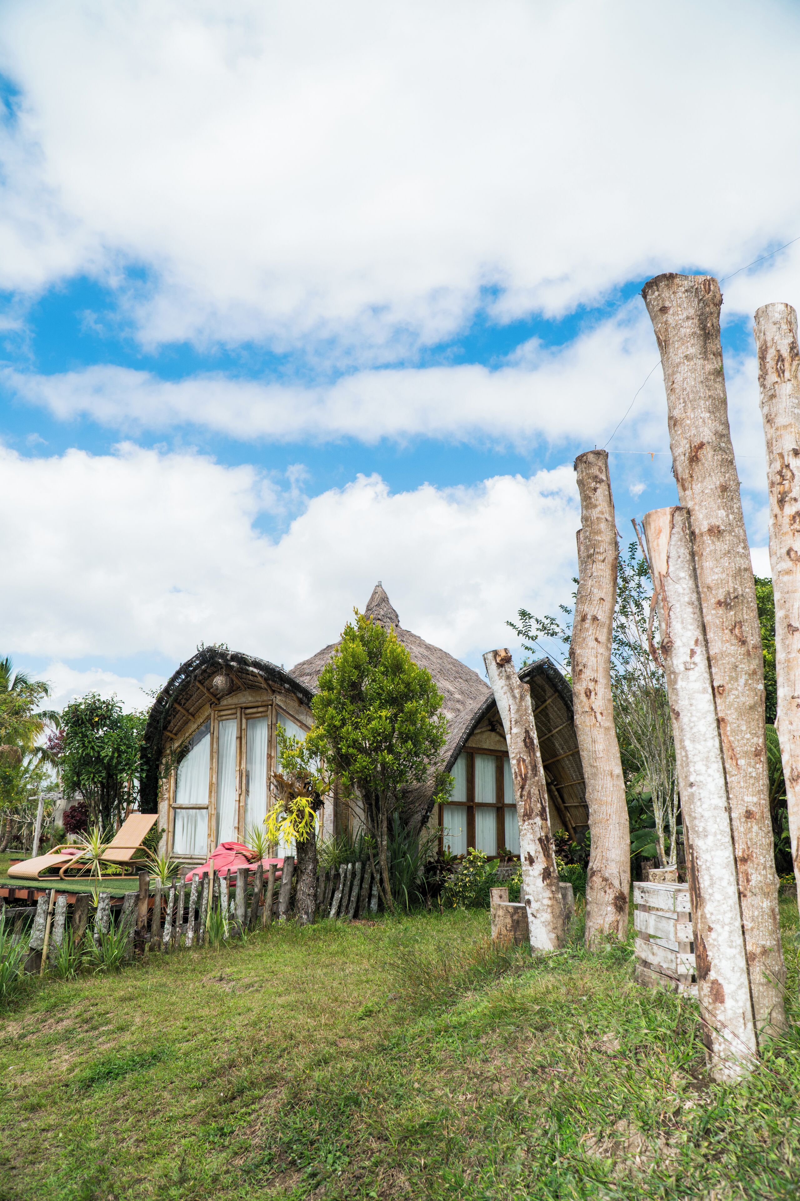 A rustic house with a thatched roof, surrounded by wooden posts and greenery.