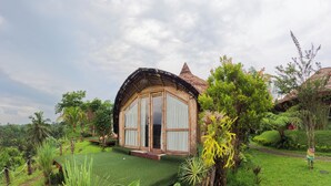 A rustic, single-story building with a thatched roof, surrounded by lush greenery and a well-maintained lawn. - Aranka Tempasan (Pringgasela)