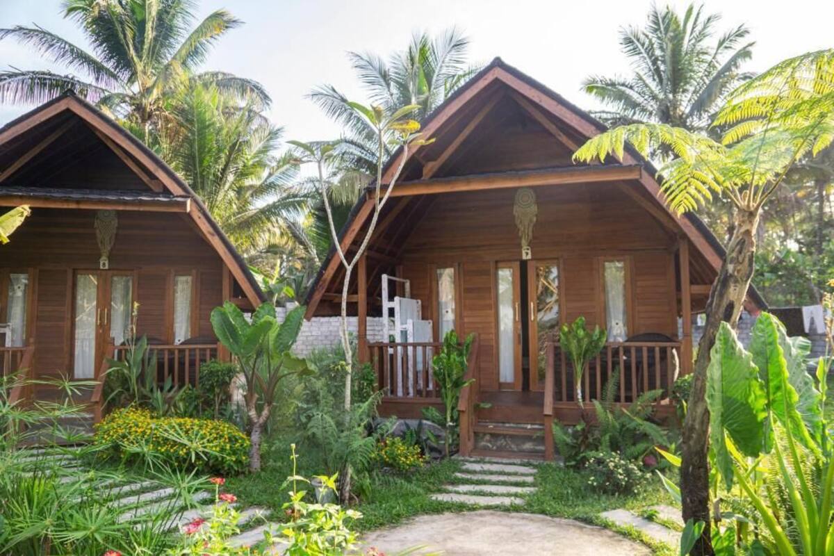 Deux cabanes en bois dotées de balcons, entourées d’une végétation tropicale et de palmiers.