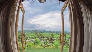 A view through a window with bamboo frames, revealing a lush green landscape with palm trees and water channels. - Aranka Tempasan (Pringgasela)