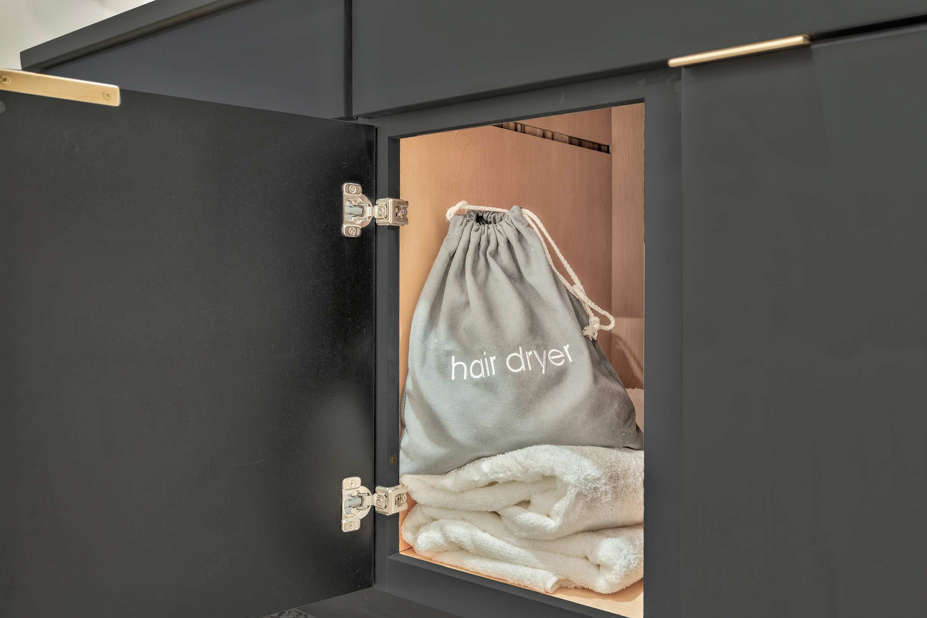 A storage cabinet with a drawstring bag labeled "hair dryer" and a stack of towels.