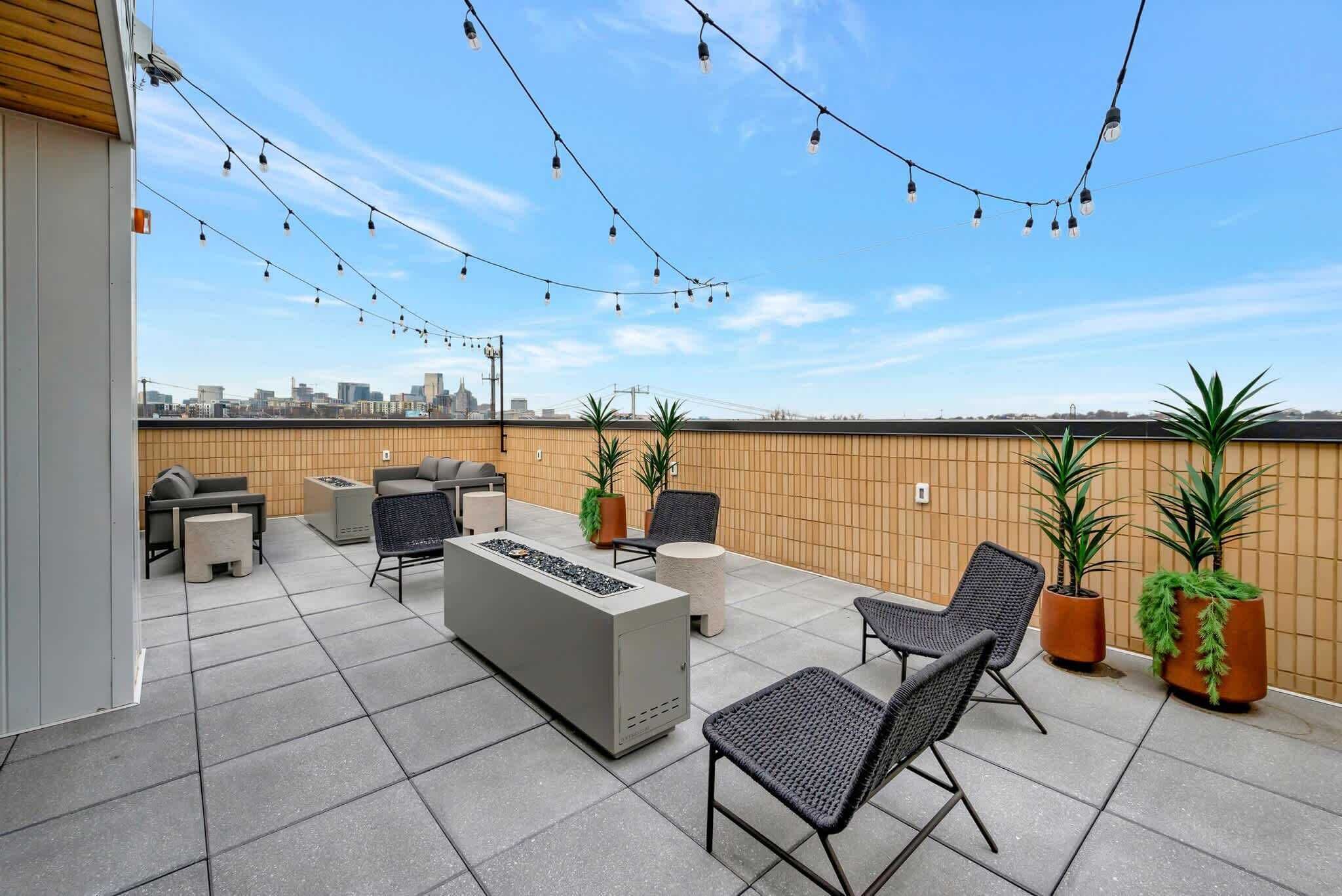 Una terraza en la azotea con mobiliario exterior, luces colgantes y plantas en macetas.