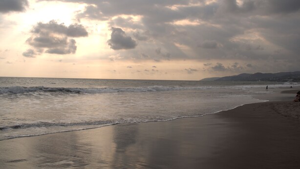 A beach with waves, a cloudy sky, and distant mountains. - Minerva Hotel and Restaurant (Playa San Blas)