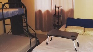 A dormitory room with bunk beds, a small table, a chair, and a window with curtains. - Minerva Hotel and Restaurant (Playa San Blas)