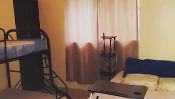 Un dormitorio con literas, una mesita, una silla y un ventanal con cortinas.