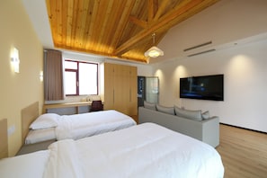Ett hotellrum med två sängar, en soffa, en TV och synliga träbjälkar i taket.