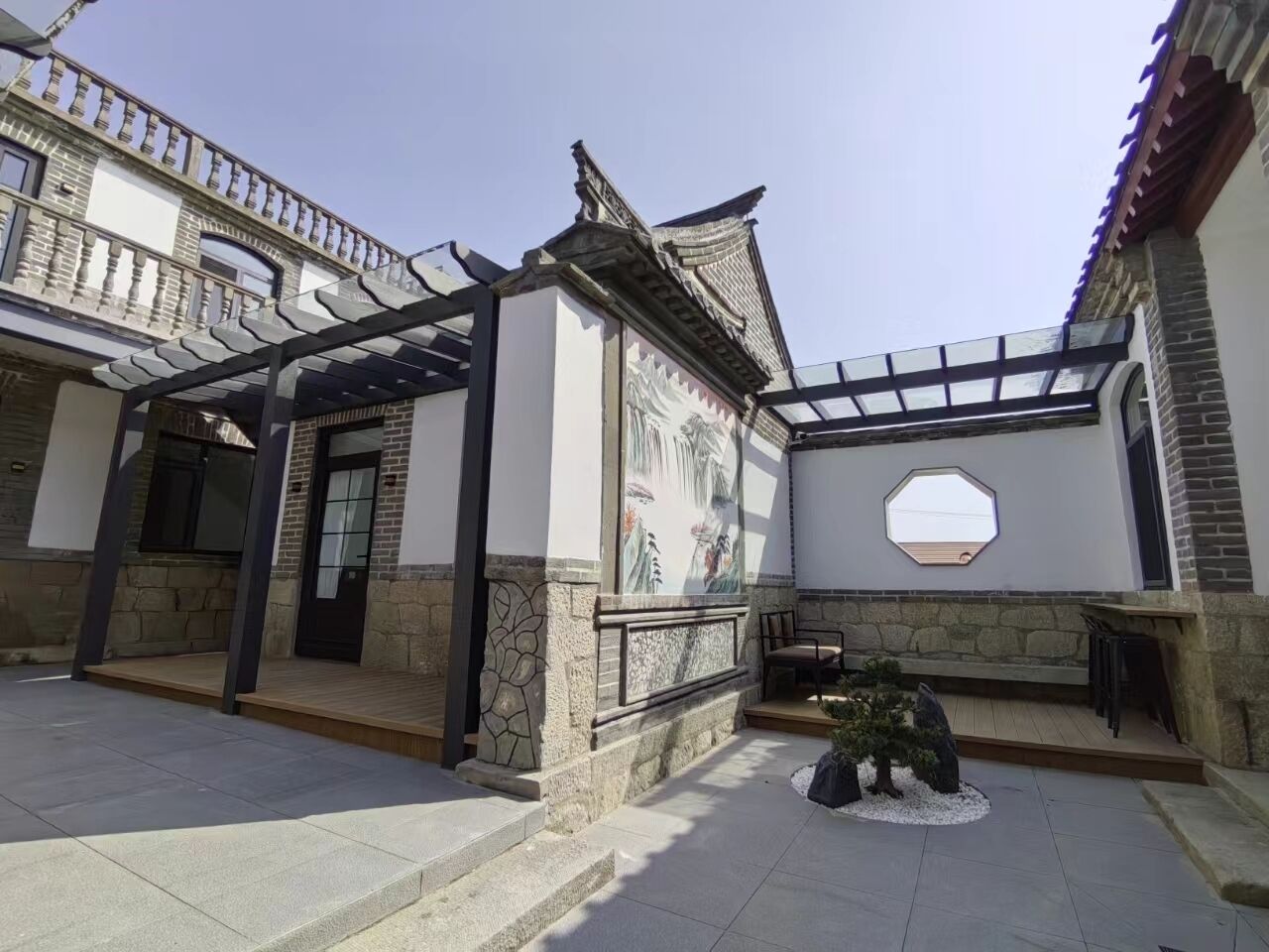 A courtyard with a traditional Chinese architectural style, including a wooden pergola and a mural.
