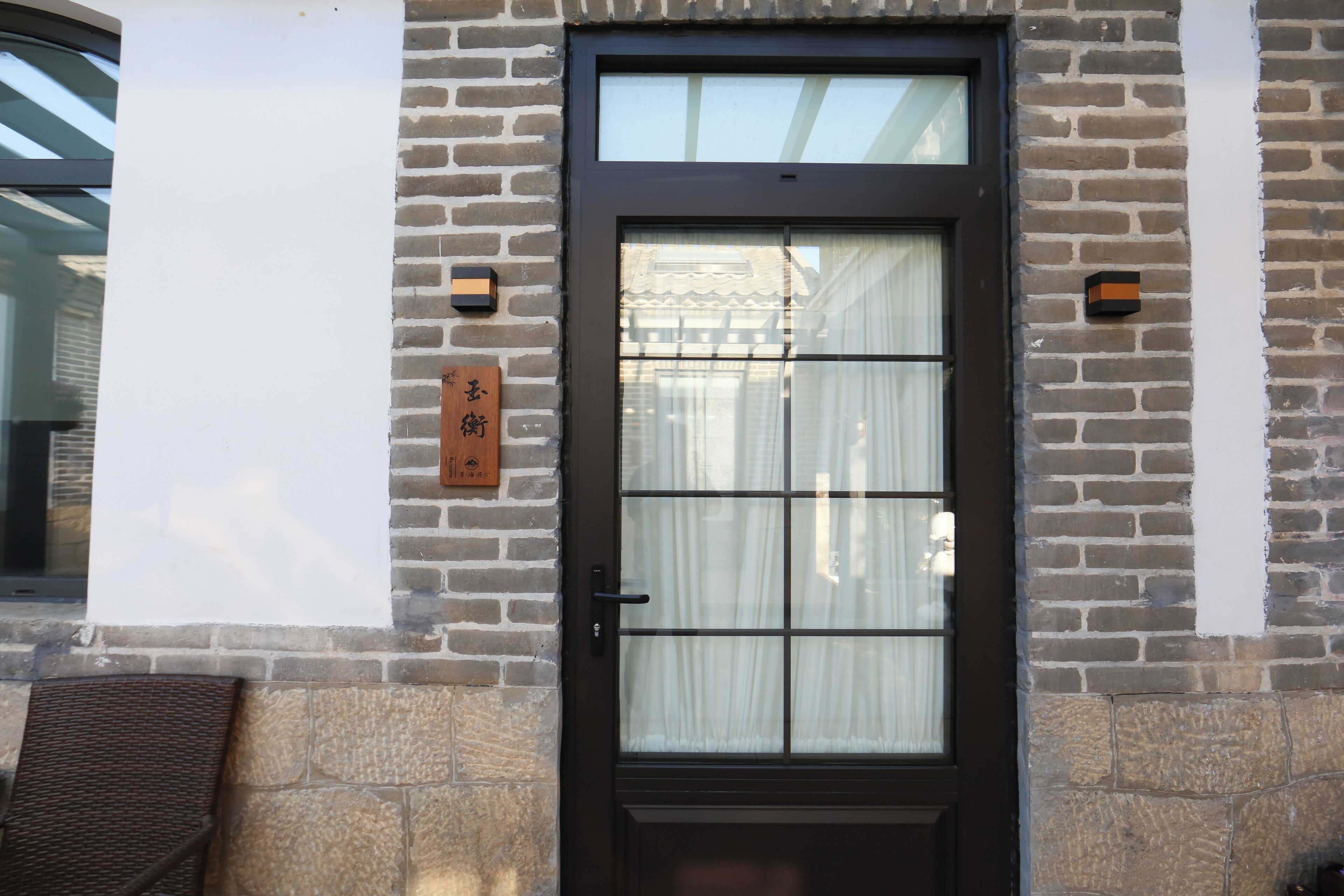 Un edificio de ladrillo con una puerta marrón oscuro, una ventana de diseño enrejado y una pequeña señal en la pared.