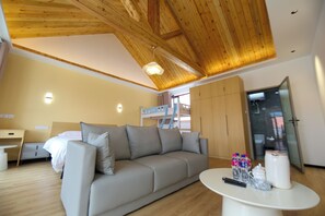 A modern room with a wooden ceiling, a sofa, a small table with a kettle, bottles, and a bed with a bunk bed in the background. - JOYSEA HUT (Yantai)