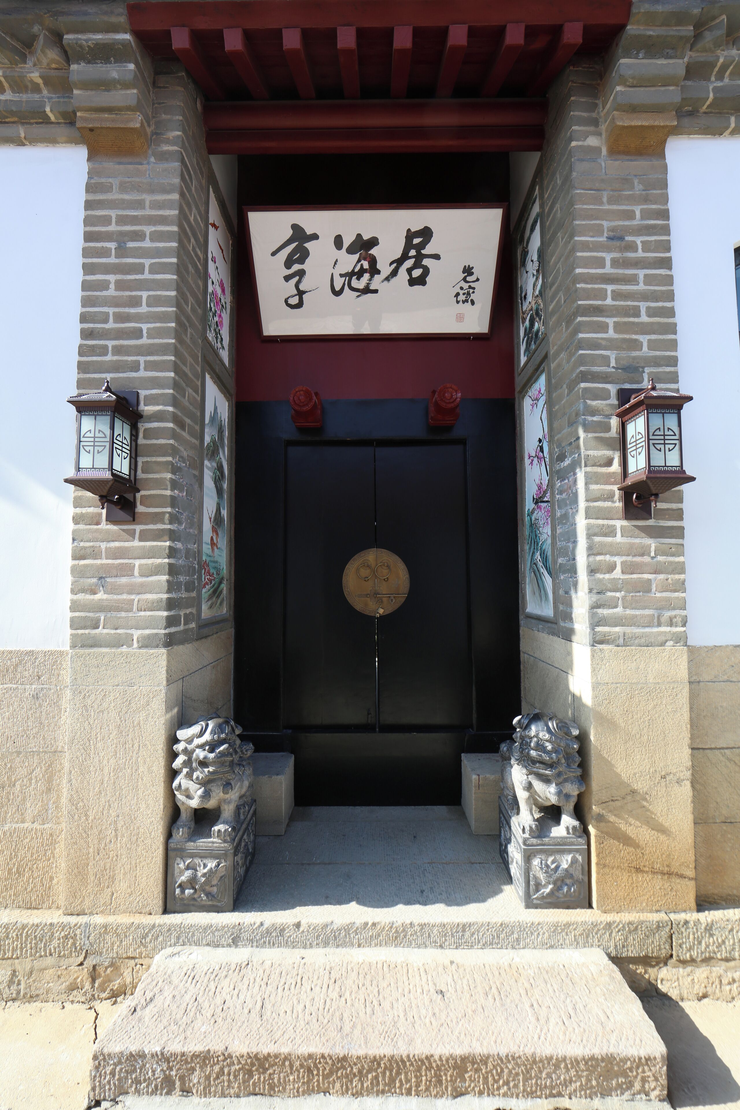 A traditional entrance with a black door, two stone lion statues, and a sign with Chinese characters.