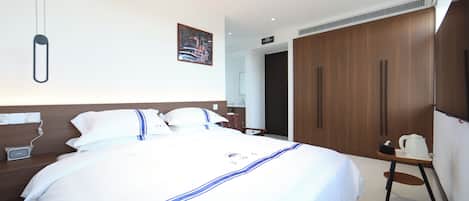 Quarto de hotel com uma cama grande, guarda-roupa de madeira, uma pequena mesa com uma chaleira e um candeeiro fixado na parede.
