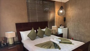 Un lit bien fait, avec du linge de lit vert et blanc, une table de chevet avec une lampe et un luminaire fixé au mur.