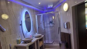 Une salle de bain moderne dotée d’un grand miroir, de deux vasques, d’une cabine de douche et d’un porte-serviettes.