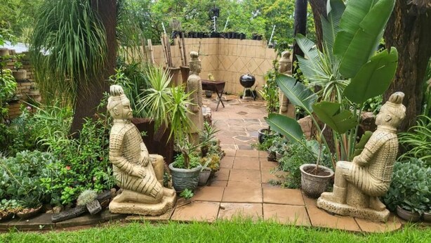 Un jardin agrémenté de deux statues en pierre, d’un mur en briques et de diverses plantes en pot.