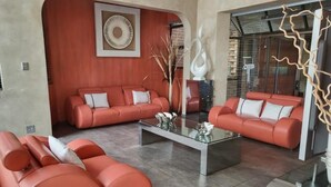 Un salon moderne avec deux canapés rouges, une table basse en verre et des éléments décoratifs, comme une œuvre d’art murale et un vase sculptural.