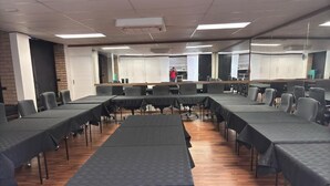 Une salle de conférence avec plusieurs tables recouvertes de nappes sombres, un plancher en bois et un mur en briques.