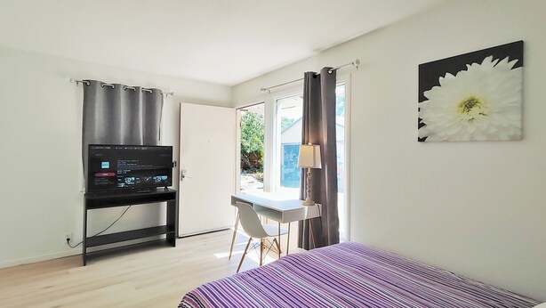 Une chambre d’hôtel comprenant un lit, un bureau avec une chaise, une télévision et une grande fenêtre avec des rideaux.