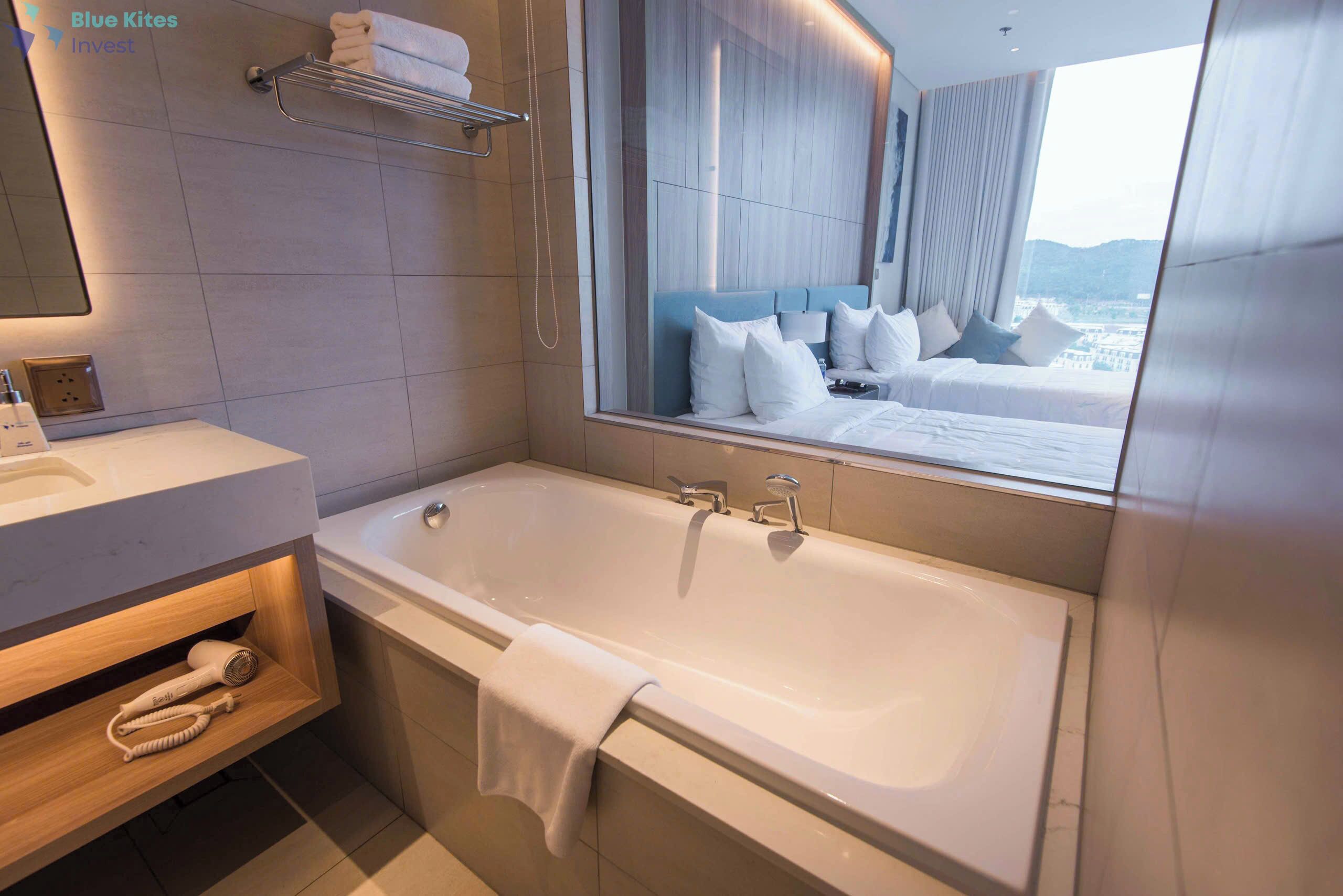 A modern bathroom with a large bathtub, a vanity with a mirror, and a view of a bedroom with a bed and pillows.
