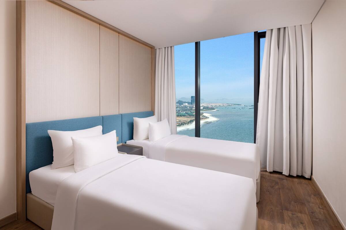 A hotel room with two beds, a view of the sea, and a cityscape.