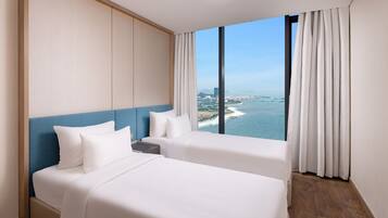 A hotel room with two beds, a view of the sea, and a cityscape.