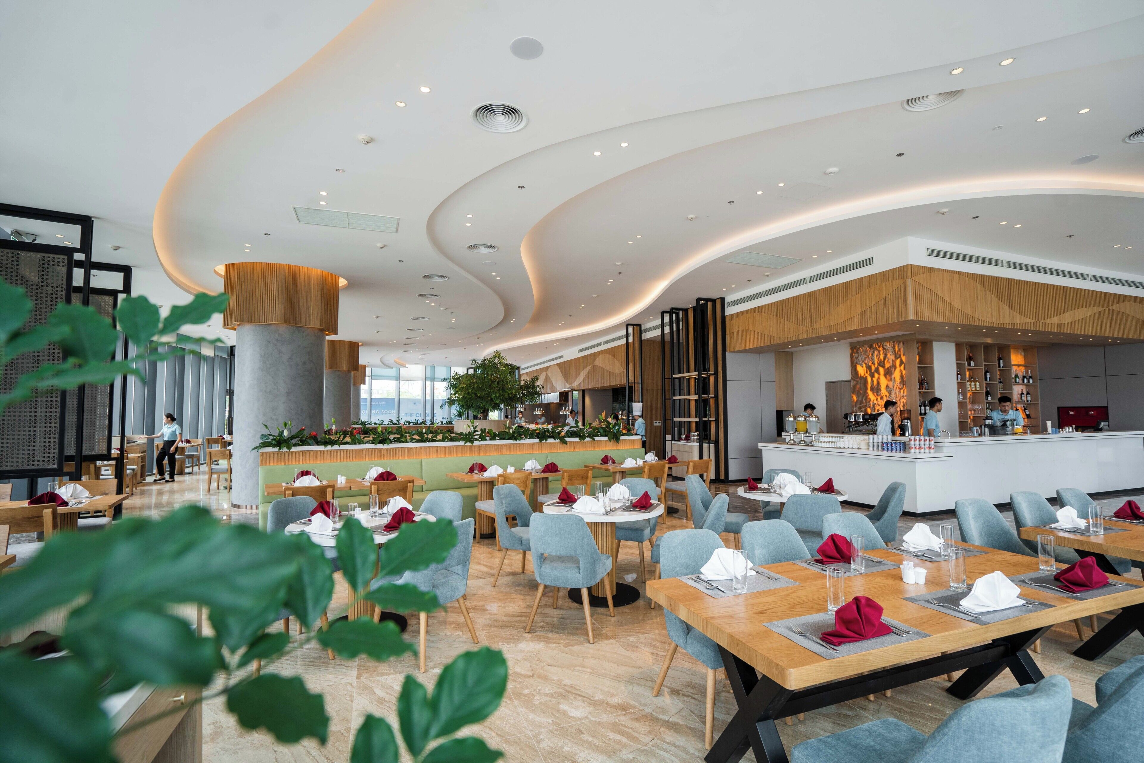 Un restaurante moderno con techo curvo, mesas y sillas de madera, y un área de bar con vistas.
