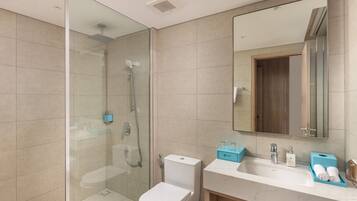 Une salle de bain moderne avec une douche en verre, des toilettes, un lavabo avec un miroir et un meuble-lavabo avec des articles de toilette.
