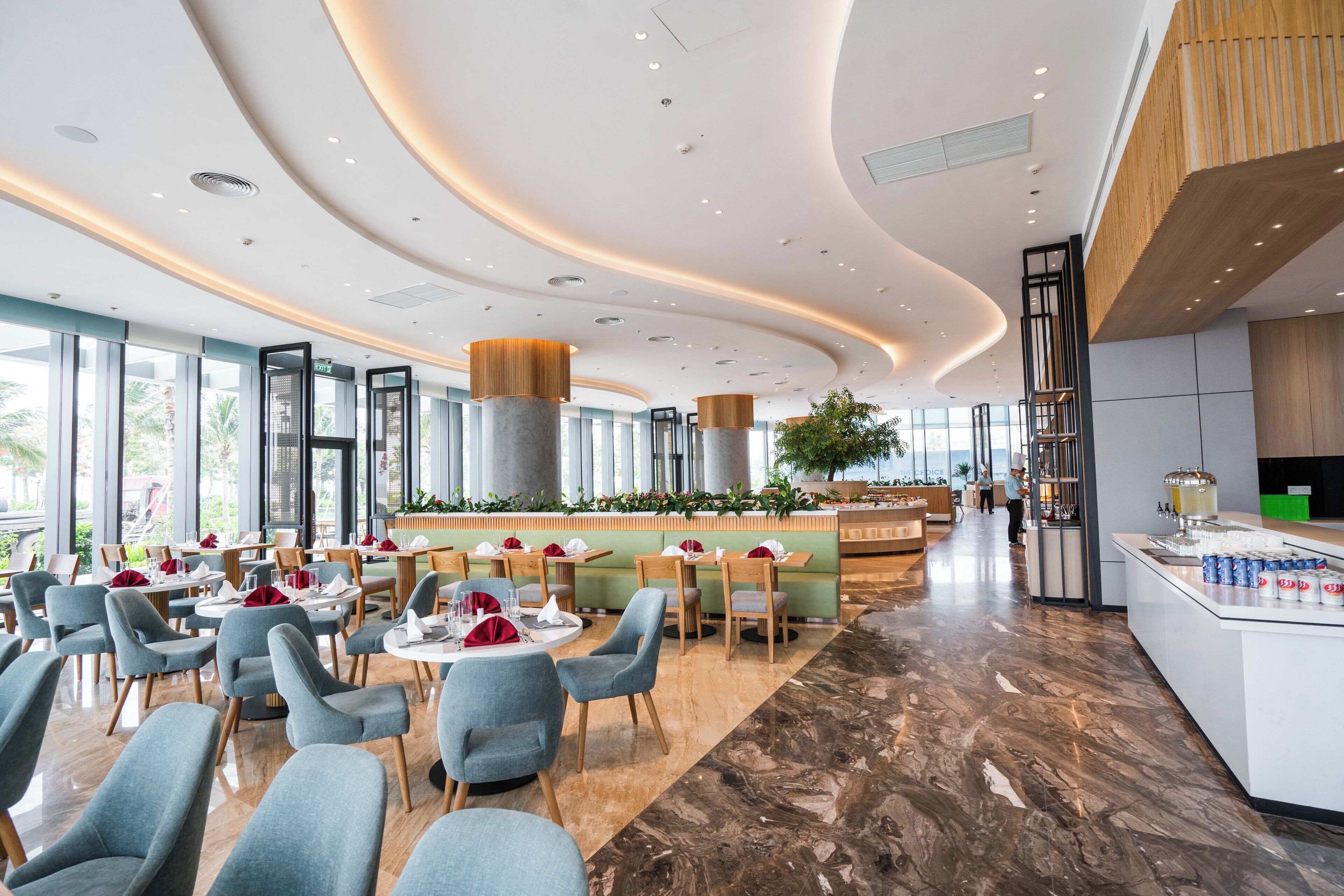 A modern restaurant with round tables, blue chairs, and a central bar area.