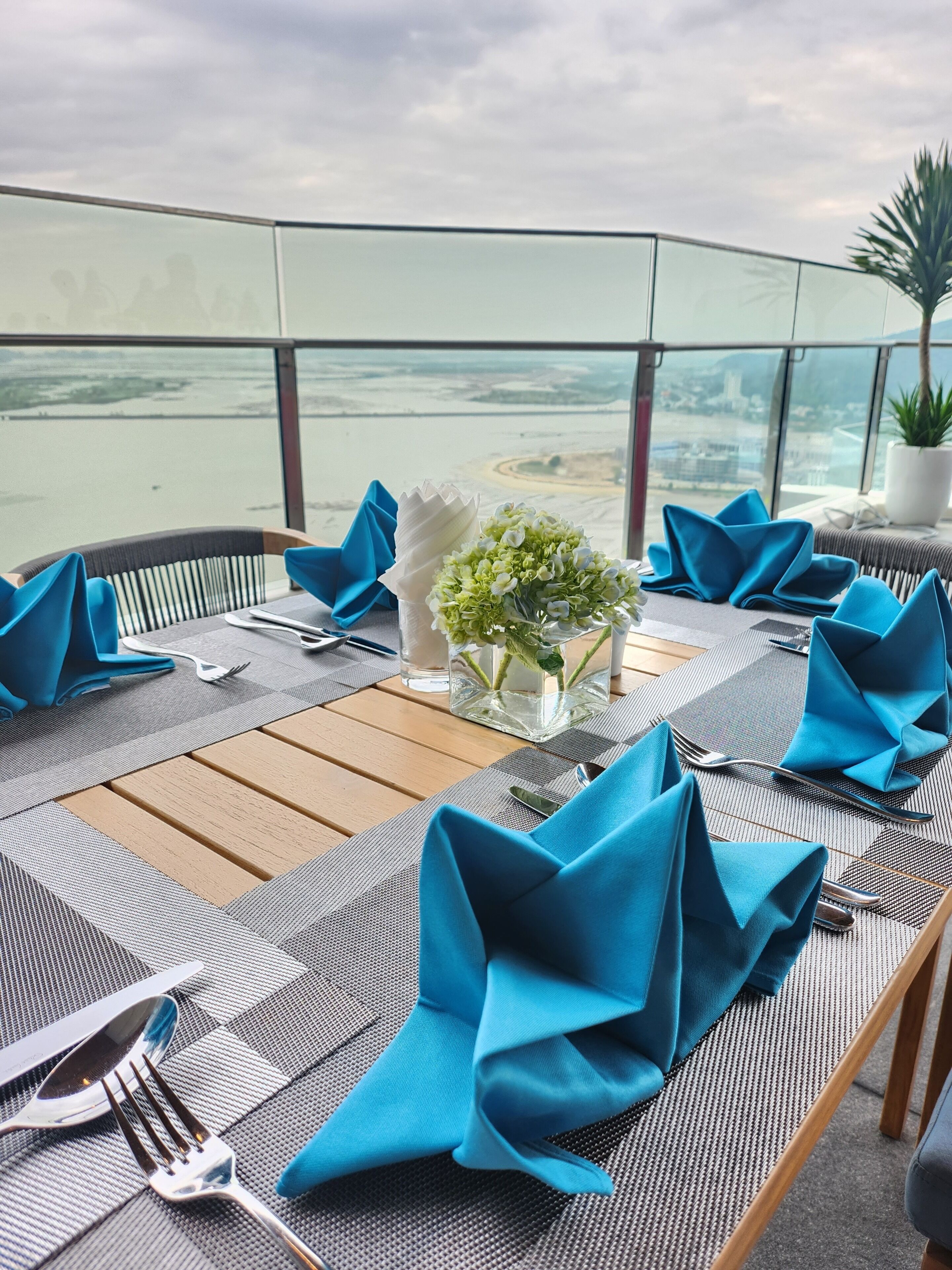 Een dakterras met een eetgedeelte, tafels voor vier personen, elk met blauwe servetten, bestek en een bloevas.