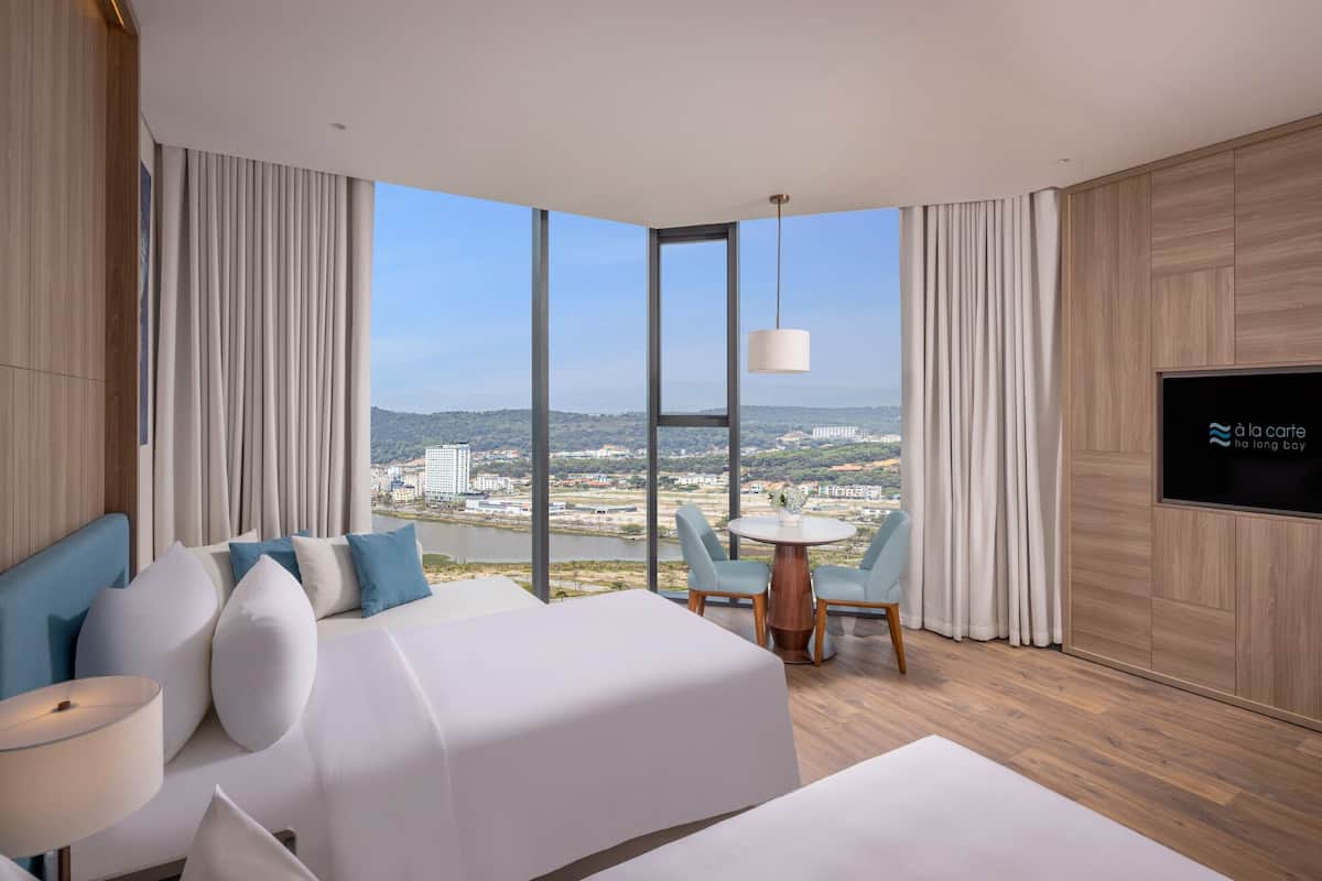 A hotel room with a large window, a bed, a small table, and a TV.
