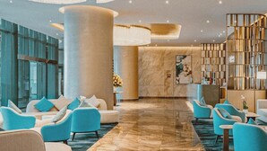 A spacious lobby with a marble floor, blue armchairs, and a large column. - Alacarte Ha Long Bay Managed by Navis Global (Bai Chay)