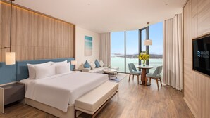A hotel room with a large bed, a sofa, a dining table with chairs, a TV, and a view of the sea. - Alacarte Ha Long Bay Managed by Navis Global (Bai Chay)