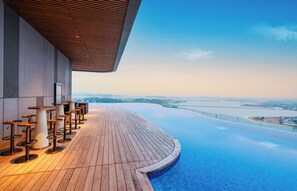 Una piscina a sfioro sul tetto con un pontile in legno e sgabelli da bar, con vista sulla città.