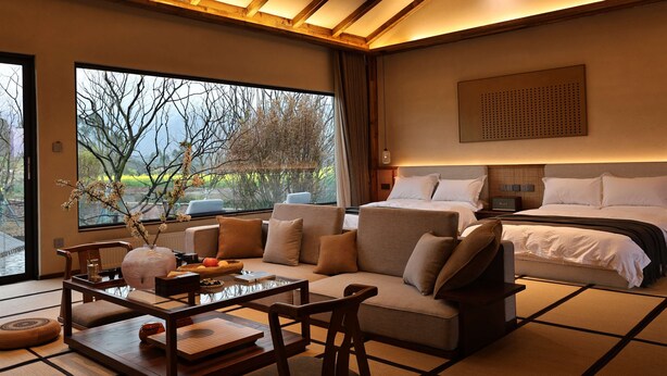 A modern hotel room with a large bed, a sofa, a dining table, and a view of trees through the window. - Miss or Dismiss (Chongqing)