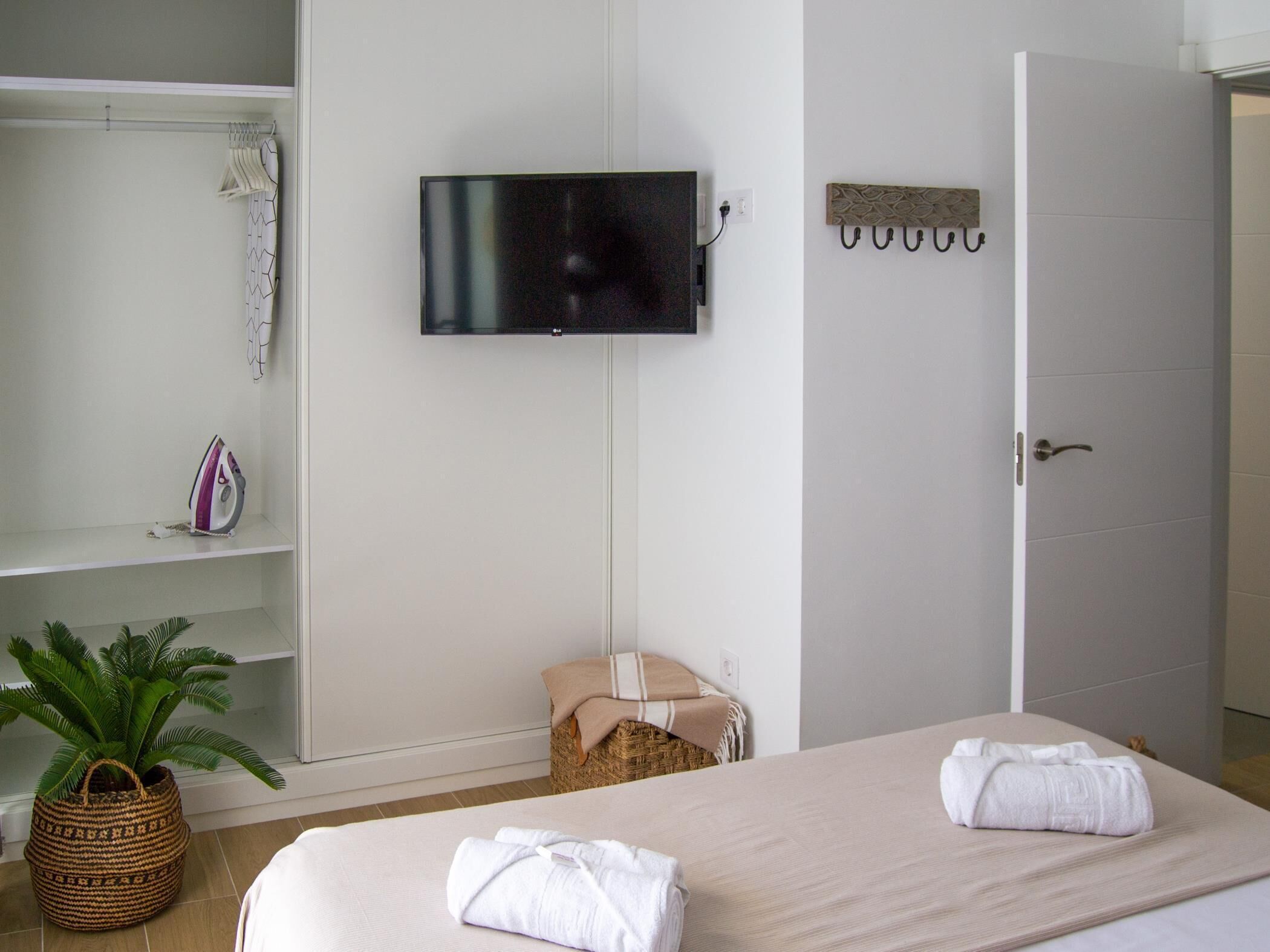 Une chambre à coucher avec un lit, un téléviseur fixé au mur, une armoire et une petite plante.