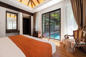 Ein Hotelzimmer mit einem großen Bett, einem Holzstuhl, Blick auf einen Swimmingpool und einem großen Fenster mit Vorhängen.