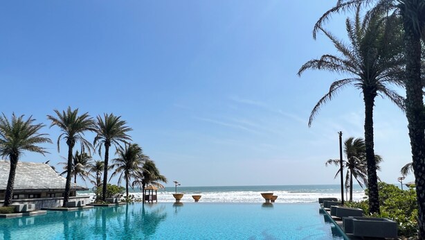 A clear blue infinity pool with a view of the ocean, surrounded by palm trees and a beachside building. - GuangPo MeiYa Homestay LingShui (Lingshui)