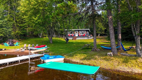 Un chalet au bord du lac, doté d’un espace extérieur aménagé et d’un quai avec des bateaux.