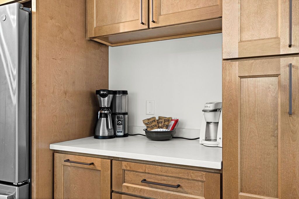 A kitchen with wooden cabinets, a stainless steel refrigerator, a coffee maker, and a bowl of coffee pods.