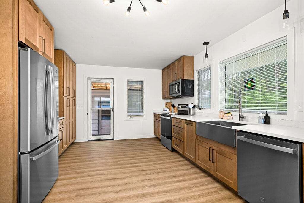 A modern kitchen with wooden cabinets, stainless steel appliances, and a large window with blinds.