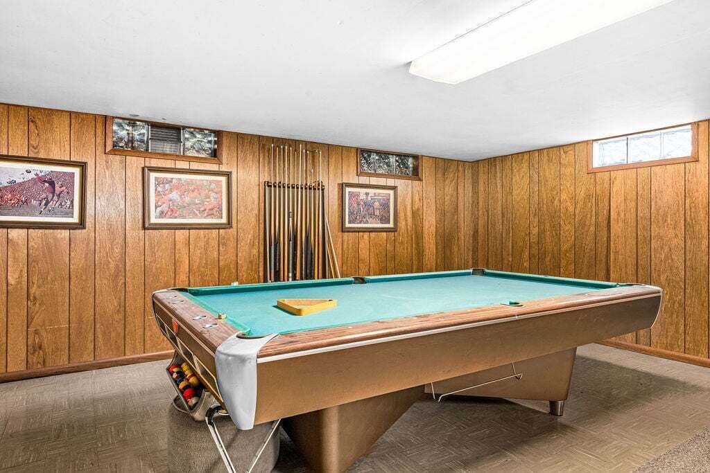 Une table de billard dans une pièce aux murs lambrés et décorée de tableaux encadrés.