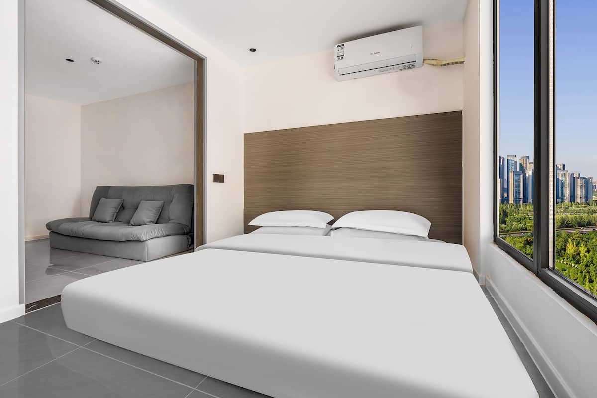 A modern hotel room with a large bed, a grey sofa, and a city view.