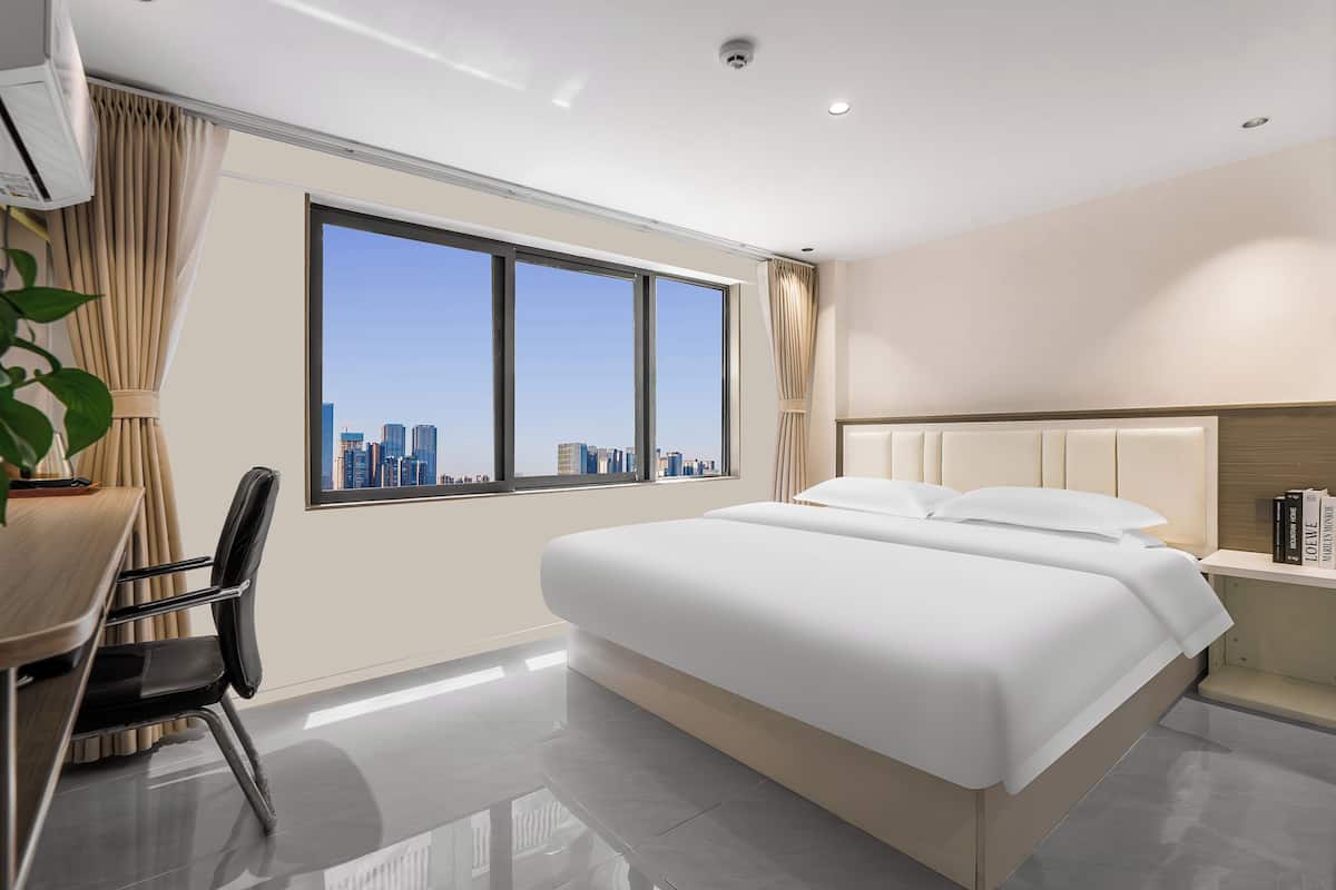 A modern hotel room with a large bed, a desk, and a view of the city skyline.