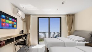 Una camera d'albergo con una grande TV a parete, una scrivania con una sedia, due letti e un balcone con vista sulla città.