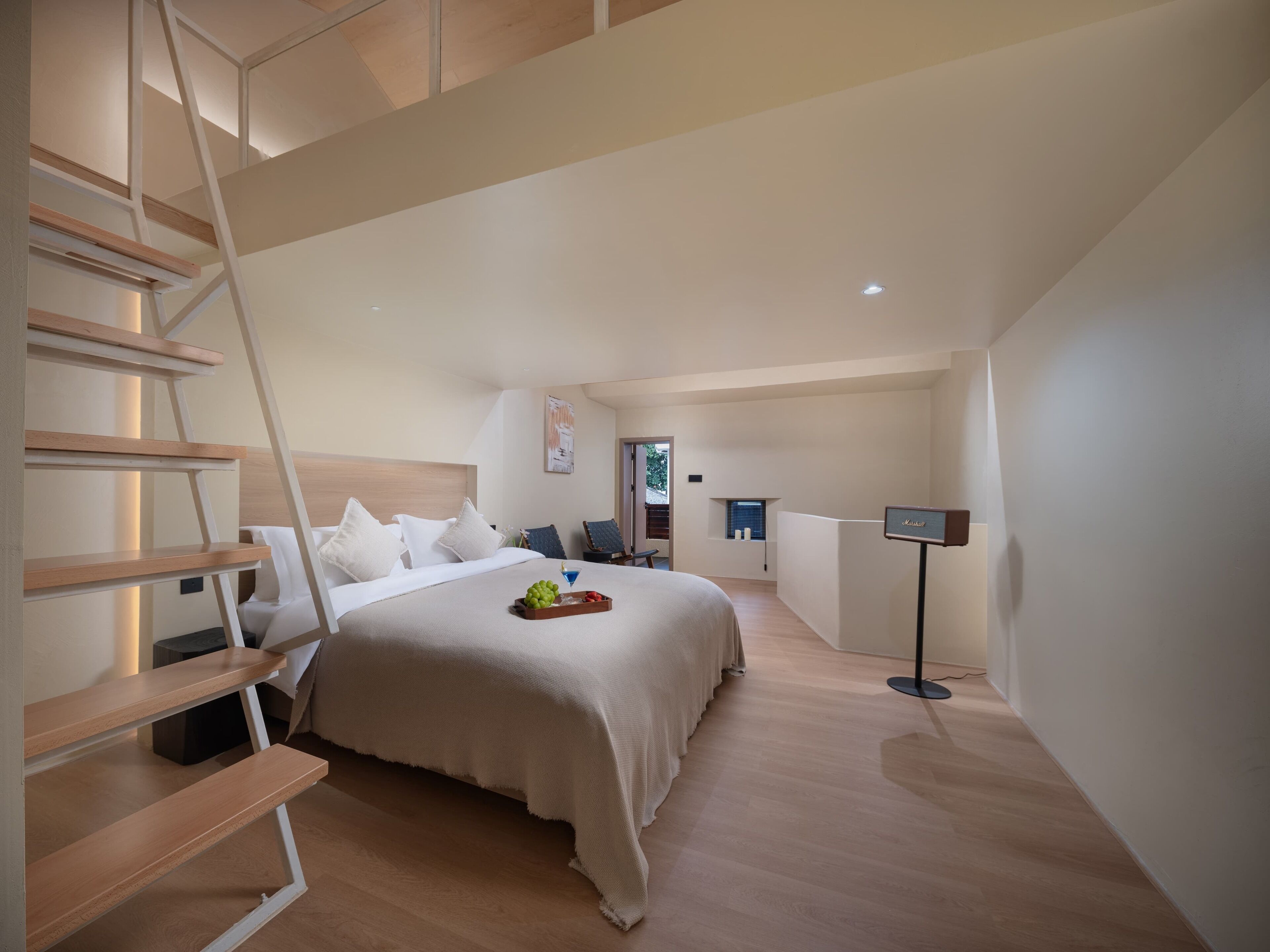 A modern hotel room with a bed, a desk, a chair, a small window, and a TV.