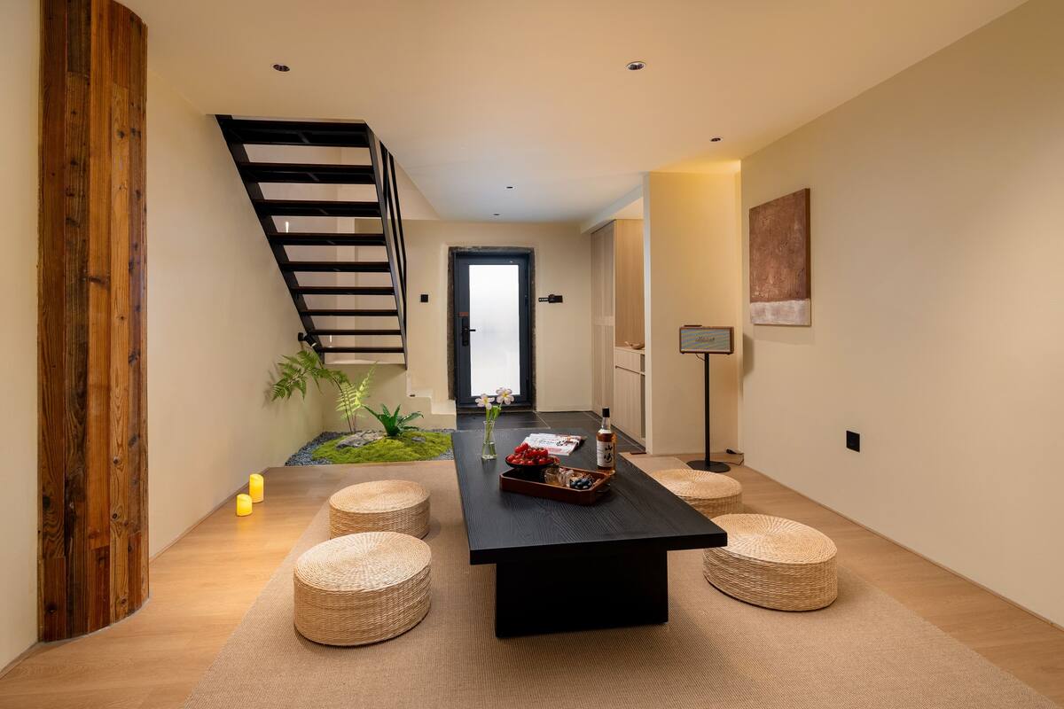 A modern interior with a black table, wicker ottomans, a staircase, and a door leading to another room.